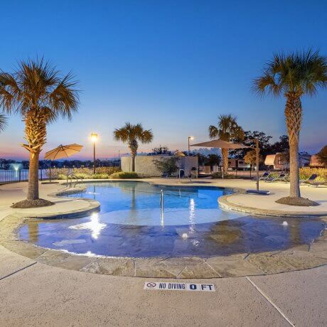 Twilight pool photo at Brazoria Lakes RV Resort with glowing blue water, palm trees, lake fountain, and hot tub in Brazoria, Texas