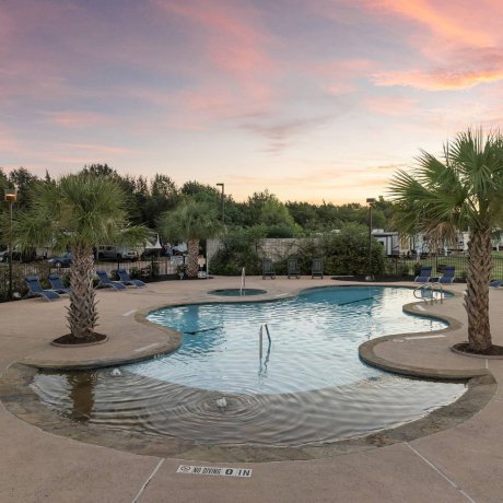 Highway 6 RV Resort twilight pool area with palm trees, lounge chairs and patio — Houston, TX pet-friendly monthly RV stays