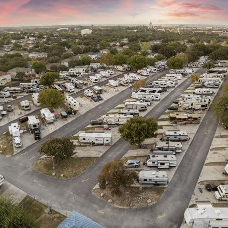 Aerial photo of Admiralty RV Resort showing organized rows of RVs with nearby homes and a theme park in the background during a colorful sunset.