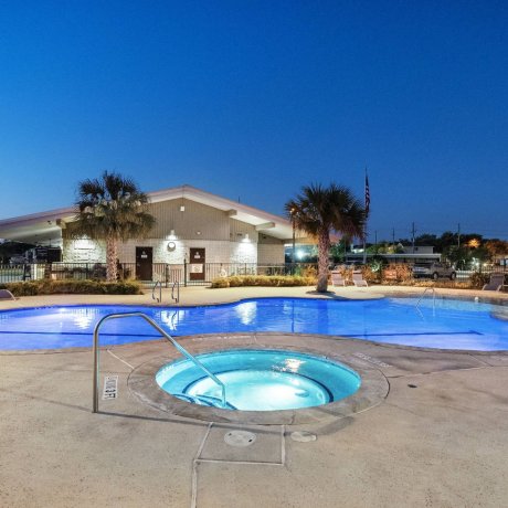 Highway 6 RV Resort pool and spa at dusk with palm trees and clubhouse in the background — Houston, TX pet-friendly monthly stays