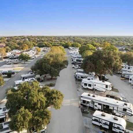Daylight aerial view of tree-lined RV sites at Admiralty RV Park in San Antonio, Texas, with wide access roads and modern campers parked throughout.