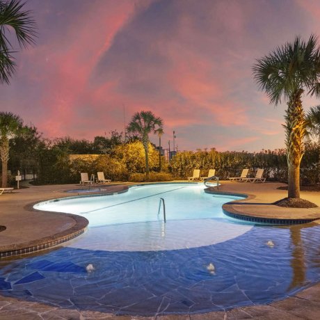 Tropical-style swimming pool with palm trees at Fallbrook RV Resort in Houston, TX, captured at twilight.