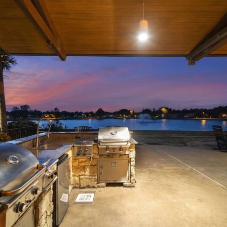 Covered outdoor kitchen and grilling station with dual stainless steel BBQs and sink, overlooking the lake and nearby fire pit at Lakeview RV Resort