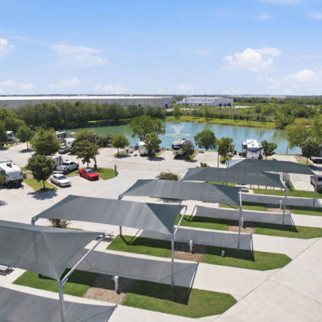 Aerial view of Southlake RV Resort featuring premium concrete pull-through sites, covered parking canopies, and luxury RVs parked around a scenic stock pond with a central water fountain.