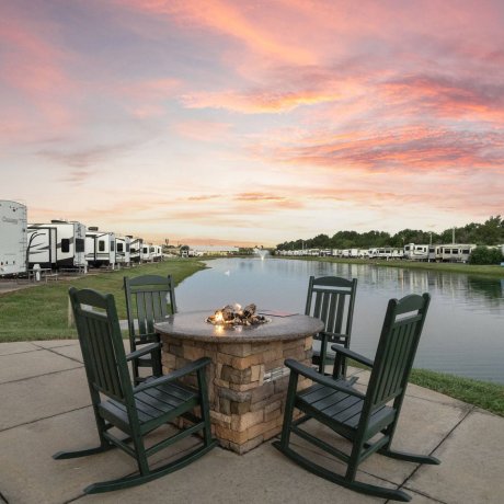 Highway 6 RV Resort lakeside fire pit with rocking chairs and long RV sites at sunset — Houston, TX pet-friendly monthly stays