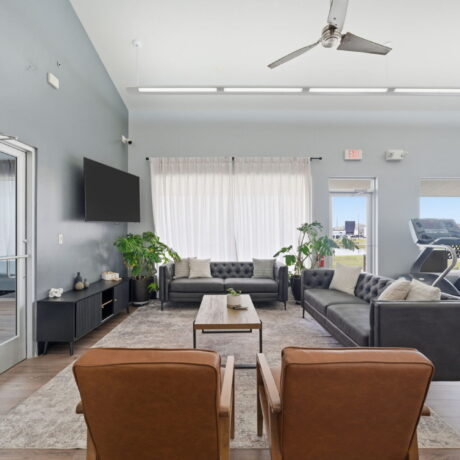 Clubhouse lounge with leather seating flat-screen TV and view into the fitness center at Mont Belvieu RV Resort near Houston Texas