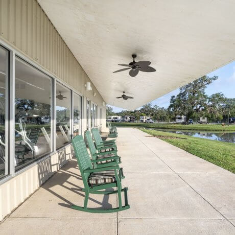 Eight green rocking chairs behind the clubhouse at Brazoria Lakes RV Resort with ceiling fans overhead and lake view in Brazoria, TX