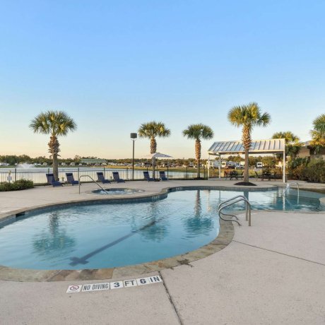 Pool at Eastlake RV Resort in Houston, TX with palm trees, clear blue skies, and lake with fountain in the background near 77044