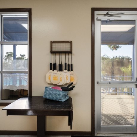 Indoor view of paddle rack and equipment at Admiralty RV Park in San Antonio, Texas, with large windows and doors overlooking the pool area.