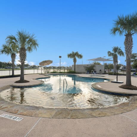 Zero-entry pool at Brazoria Lakes RV Resort with palm trees and lake in the background in Brazoria, TX