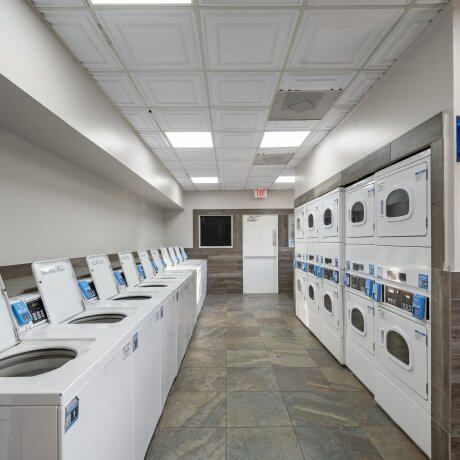Spacious laundry facility at Admiralty RV Park in San Antonio, Texas, with rows of white washers and stacked dryers on tiled flooring under bright ceiling lights.