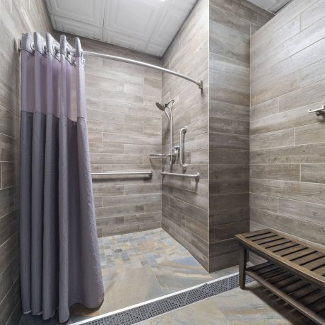 Immaculate, accessible community shower room with modern wood-look tile, grab bars, and a changing bench at Lakeview RV Resort