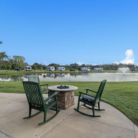 Fire pit with three rocking chairs at the clubhouse of Brazoria Lakes RV Resort, overlooking the lake and fountain in Brazoria, TX