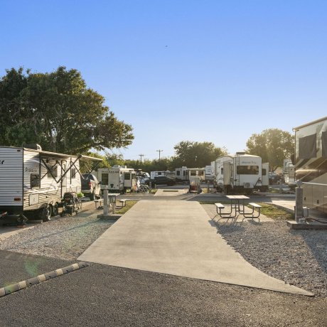 Ground-level view of a vacant RV site at Admiralty RV Park in San Antonio, Texas, with full hookups, picnic table, paved pad, and RVs parked nearby.