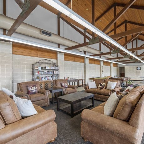 Clubhouse interior with comfortable leather lounge seating, exposed wood beams, reading nook, billiards table, and fitness center equipment at Lakeview RV Resort