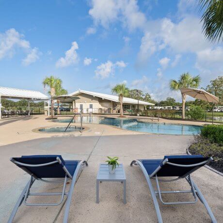View from two blue lounge chairs facing the pool and clubhouse at Brazoria Lakes RV Resort in Brazoria, TX