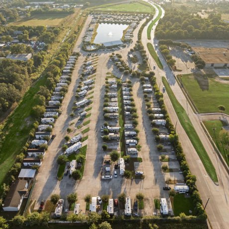 Aerial view of Fallbrook RV Resort in Houston, TX showcasing spacious RV pads, tree-lined rows, and a central fishing lake.
