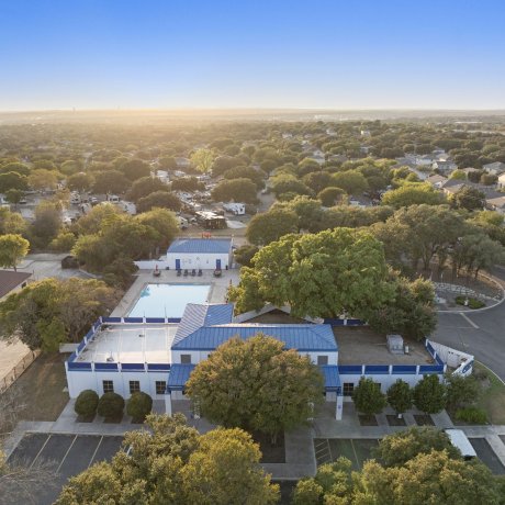 Drone view of Admiralty RV Park in San Antonio, Texas, at sunrise, featuring the clubhouse with blue roof, swimming pool, RV lots, and surrounding residential neighborhood.