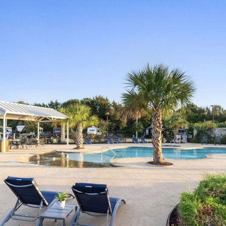 Highway 6 RV Resort sunny pool deck with lounge chairs, shaded pavilion and palm trees — Houston, TX pet-friendly monthly RV stays