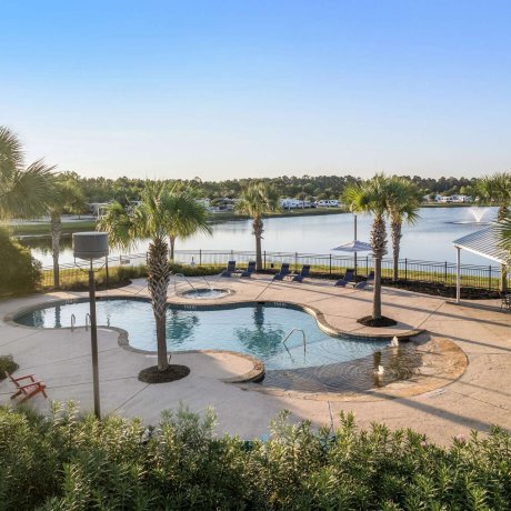 Bright poolside photo at Eastlake RV Resort in Houston, TX with lounge chairs, palm trees, hot tub, and lake fountain under clear blue skies