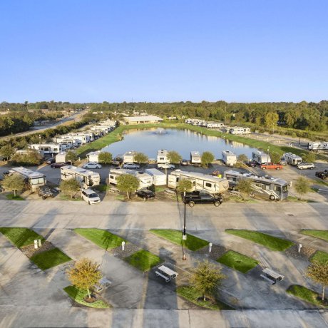 RV sites overlooking lake with fountain at Fallbrook RV Resort in Houston, TX, surrounded by greenery and paved roads.