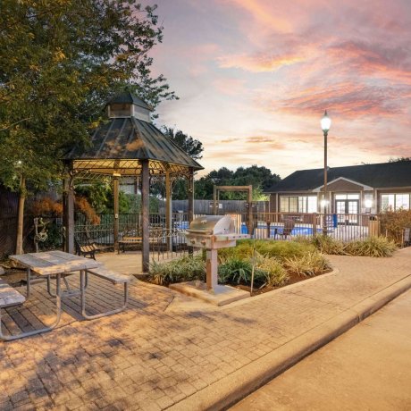 Gazebo with grill, picnic table, and pool at Allstar RV Resort in Houston, TX at sunset