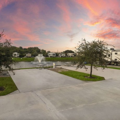 Concrete RV pad with picnic table by lake fountain at Fallbrook RV Resort in Houston, TX.