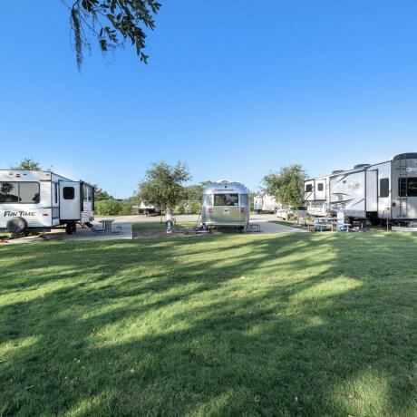 Grassy lawn facing back-in RV sites with three RVs at Brazoria Lakes RV Resort in Brazoria, TX