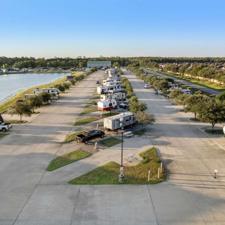 View down RV site row at Eastlake RV Resort in Houston, TX with pull-thru sites in the middle, back-in sites on each side, and blue sky above a quiet neighborhood near 77044