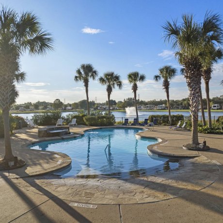 Sunny view of a swimming pool and hot tub overlooking a fishing lake with a fountain at Lakeview RV Resort by Quality RV Resorts