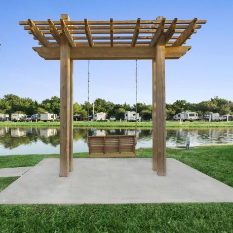 Highway 6 RV Resort lakeside pergola swing overlooking the fountain and full-hookup RV sites — Houston, TX pet-friendly monthly stays