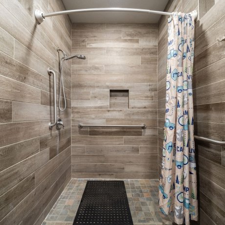 Accessible private shower stall with handrails, non-slip mat, and tiled walls at Admiralty RV Park in San Antonio, Texas.