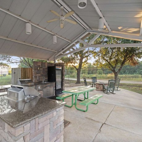Covered outdoor BBQ and picnic pavilion with granite countertops, rocking chairs, and fire pit at Allstar RV Resort in Houston, TX