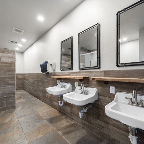 Well-lit restroom at Admiralty RV Park featuring modern sinks, mirrors, and wood-tone tile walls in San Antonio, TX.