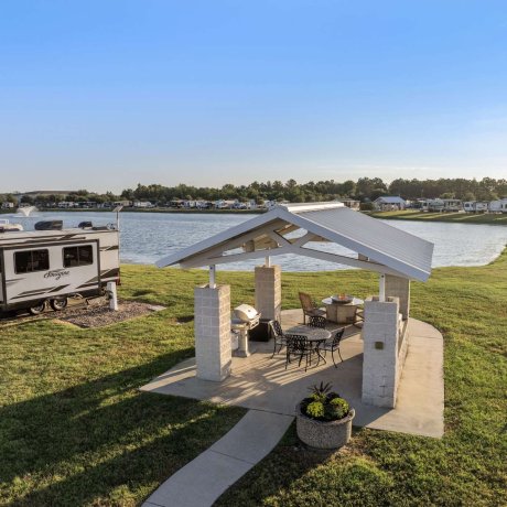 Lakeside BBQ area at Eastlake RV Resort in Houston, TX with firepit, picnic space, and nearby RV sites by the lake