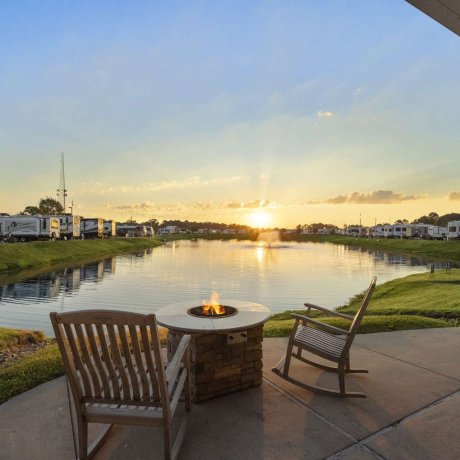 Lakeside fire pit with chairs overlooking sunset and RVs at Fallbrook RV Resort in Houston, TX.