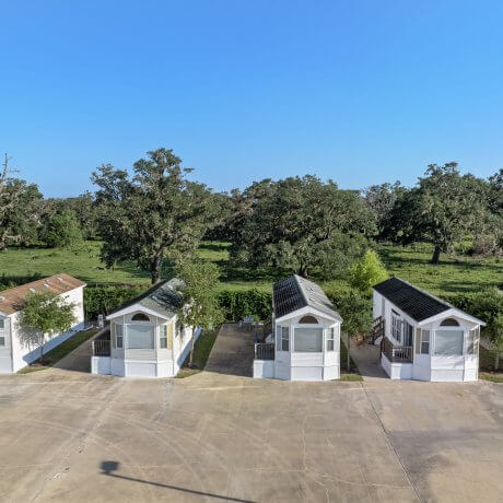 Aerial view of six park model rentals at Brazoria Lakes RV Resort with trees and open pasture behind them