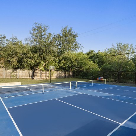 Outdoor dual-purpose court at Admiralty RV Park with pickleball nets and basketball hoop surrounded by trees in San Antonio, TX.