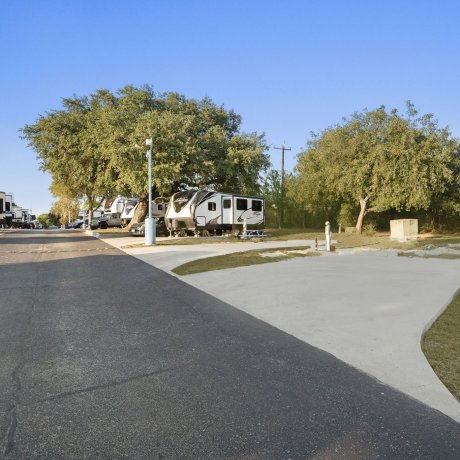 Empty concrete pull-through RV site at Admiralty RV Park with full hookups and shaded surroundings.