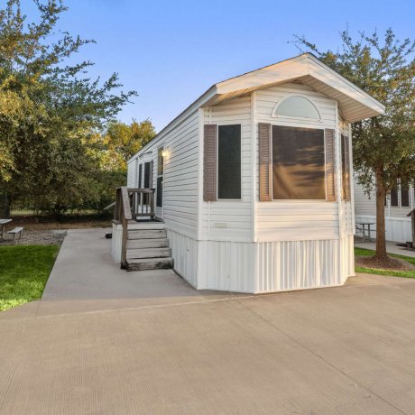 Park model rental unit at Fallbrook RV Resort in Houston, TX, with private steps, mature trees, and picnic table.