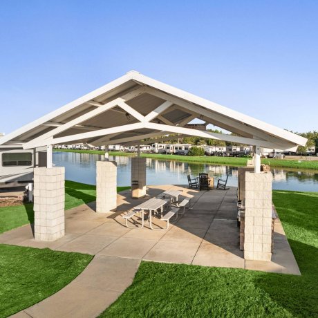 Shaded lakeside pavilion with picnic tables, grills and rocking chairs at Highway 6 RV Resort — Houston, TX outdoor pavilion for monthly RV stays
