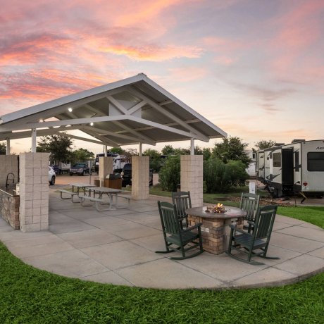 Highway 6 RV Resort covered picnic pavilion with stone fire pit and rocking chairs — Houston, TX pet-friendly monthly RV stays