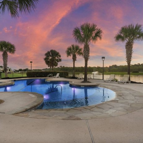 Twilight photo of resort-style pool at Westlake RV Resort in Houston TX overlooking a lake with palm trees and lounge chairs