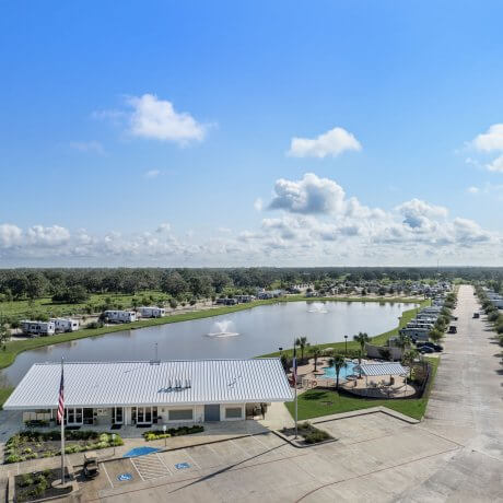 Aerial view of Brazoria Lakes RV Resort entrance with lake, RV pads, fountains, pool, and clubhouse under a blue sky