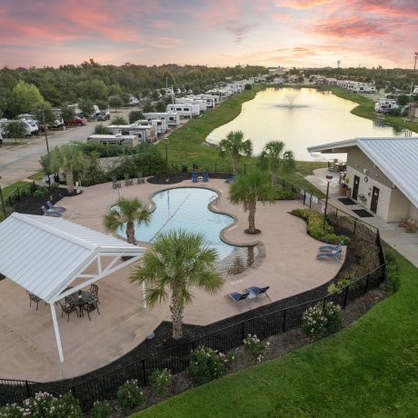 Aerial twilight view of Highway 6 RV Resort pool and long lakeside RV sites with fountain and palm trees — Houston, TX pet-friendly monthly stays