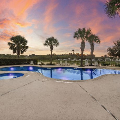 Twilight view of pool and hot tub at Westlake RV Resort in Houston, TX with palm trees and RVs in background