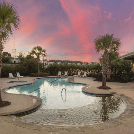 Resort-style pool and spa surrounded by palm trees at Fallbrook RV Resort in Houston, TX during sunset.