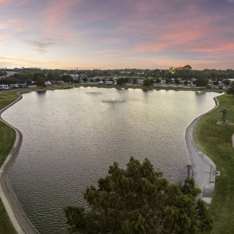 Aerial view of a large private fishing lake and walking trail at Lakeview RV Resort, with the Houston city skyline visible on the horizon at sunset