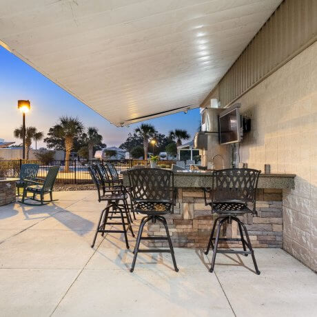 BBQ area behind the clubhouse at Brazoria Lakes RV Resort with TV, ice machine, bar seating, and firepit in the background in Brazoria, Texas