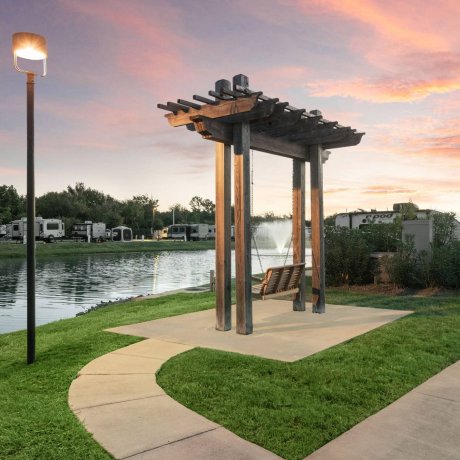 Highway 6 RV Resort lakeside pergola swing overlooking fountain and RV sites at twilight — Houston, TX pet-friendly monthly stays
